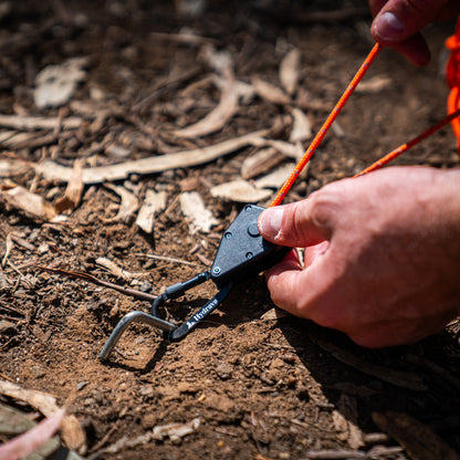 Orange Hydrava camping tensioner clipped to a camping peg.
