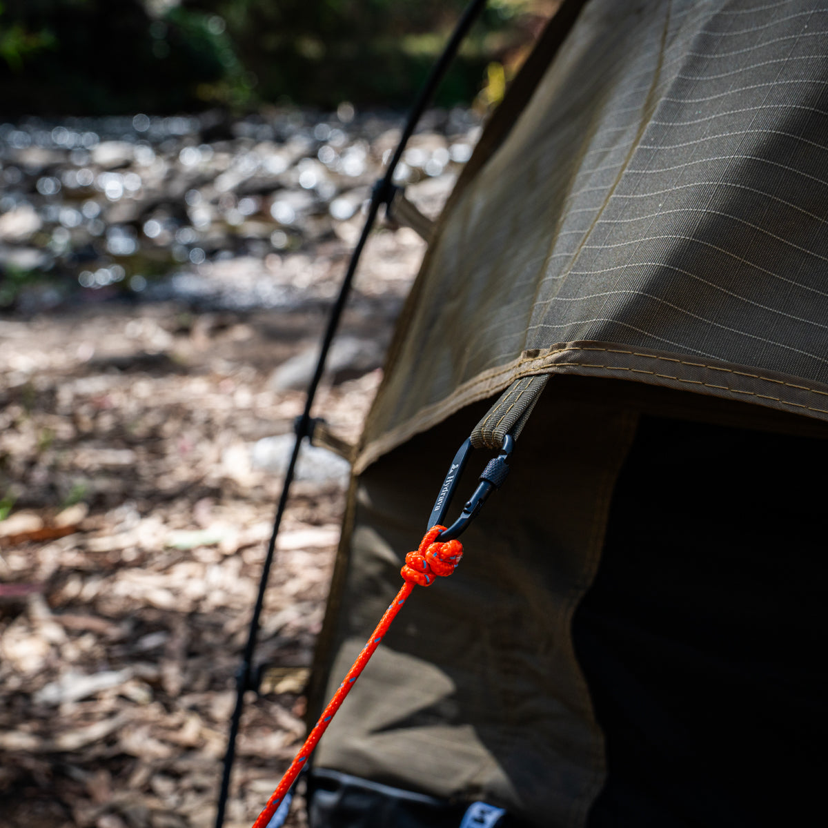 Orange Hydrava camping tensioner clipped to a guy rope on a green swag tent.